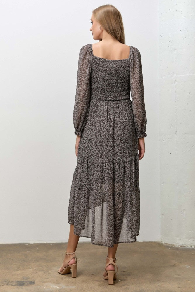 woman wearing a flowy black and beige floral maxi dress with long sleeves and a tiered skirt, shown from the back