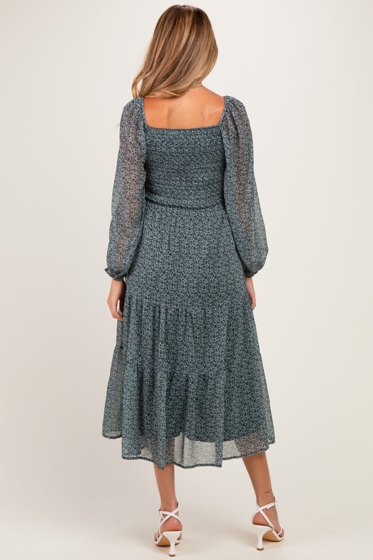 woman wearing a teal maternity dress with puff sleeves and a tiered skirt, showing a subtle baby bump