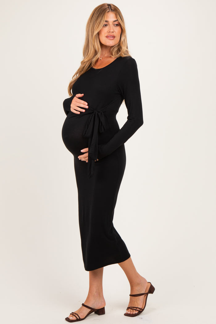 woman wearing a black long sleeve maternity dress with a tie waist and holding her baby bump