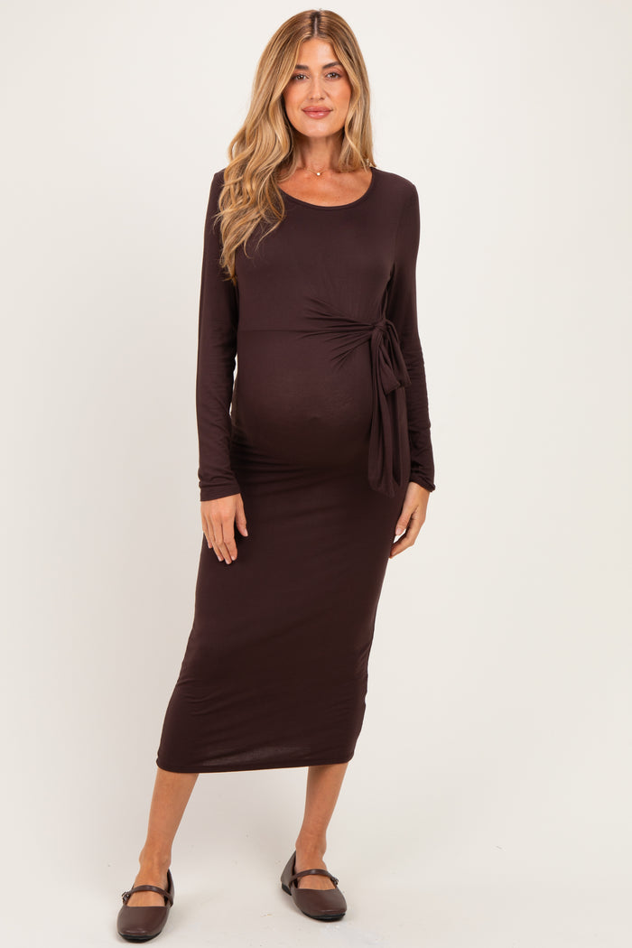 woman wearing a dark brown maternity dress with a side tie detail and long sleeves, showcasing her baby bump
