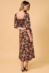 woman wearing a floral mid-length dress with smocked back and puff sleeves, standing against a beige background