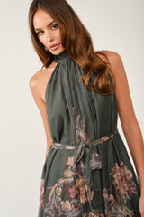 woman wearing a dark green halter neck dress with floral print and a tied waist detail