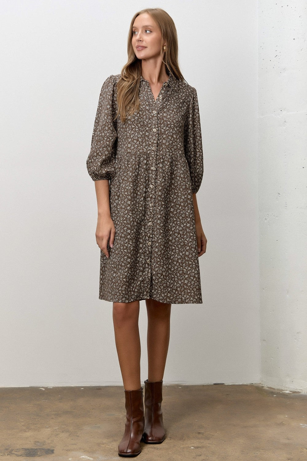 woman wearing a brown floral button-up dress with puffed sleeves and standing on a concrete floor