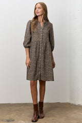 woman wearing a brown floral button-up dress with puffed sleeves and standing on a concrete floor