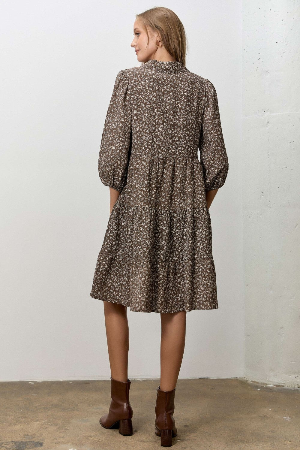 woman wearing a brown floral print tiered dress with puff sleeves and ankle boots, standing with her back to the camera