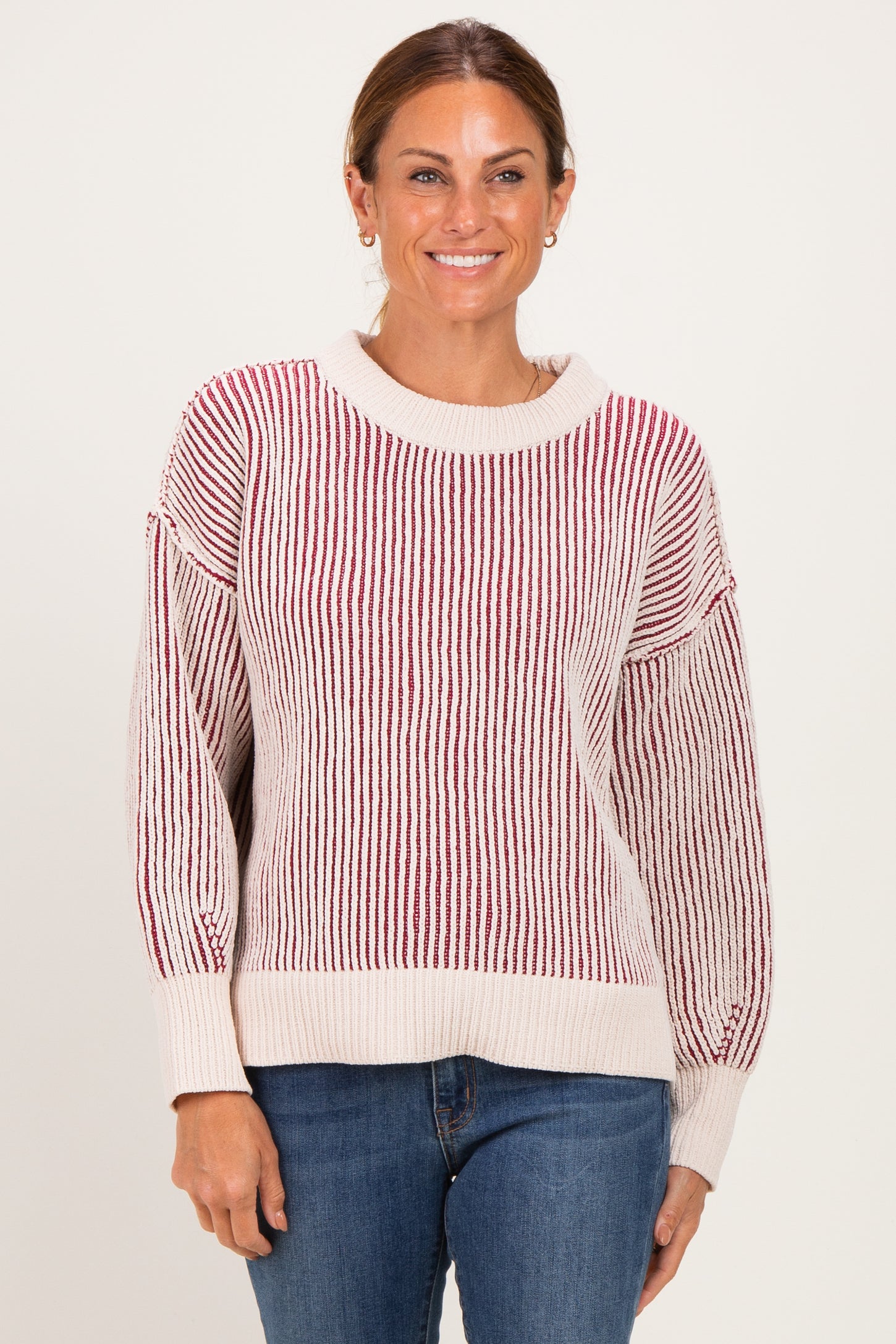 woman wearing a cream and red striped knit sweater with a relaxed fit and ribbed details, paired with blue jeans