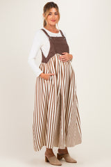 woman wearing a brown and white striped maternity dress with adjustable straps and pockets, showcasing her baby bump