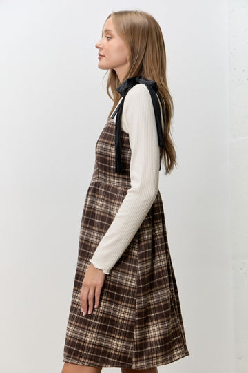 woman wearing a brown plaid dress with a flared skirt and a white long sleeve top with black ribbon details