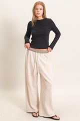 woman wearing a black long sleeve top with asymmetrical design and light beige wide-leg pants with drawstring waist