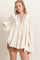 woman wearing a cream ruffled blouse with lace detailing and long sleeves, paired with a brown mini skirt