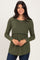 woman wearing a dark green long sleeve ribbed top with a fitted bodice and flowy bottom, smiling at the camera