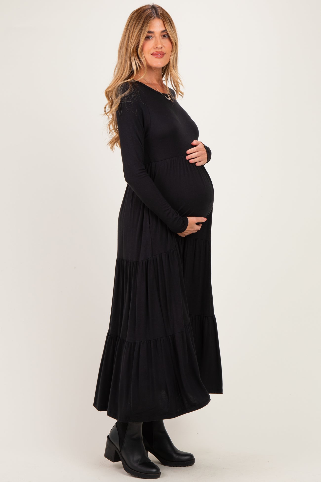 woman wearing a black long sleeve maternity maxi dress with tiered ruffles and holding her baby bump