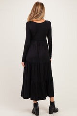 woman wearing a black long sleeve maternity dress with a tiered skirt and a relaxed fit, standing with her back to the camera