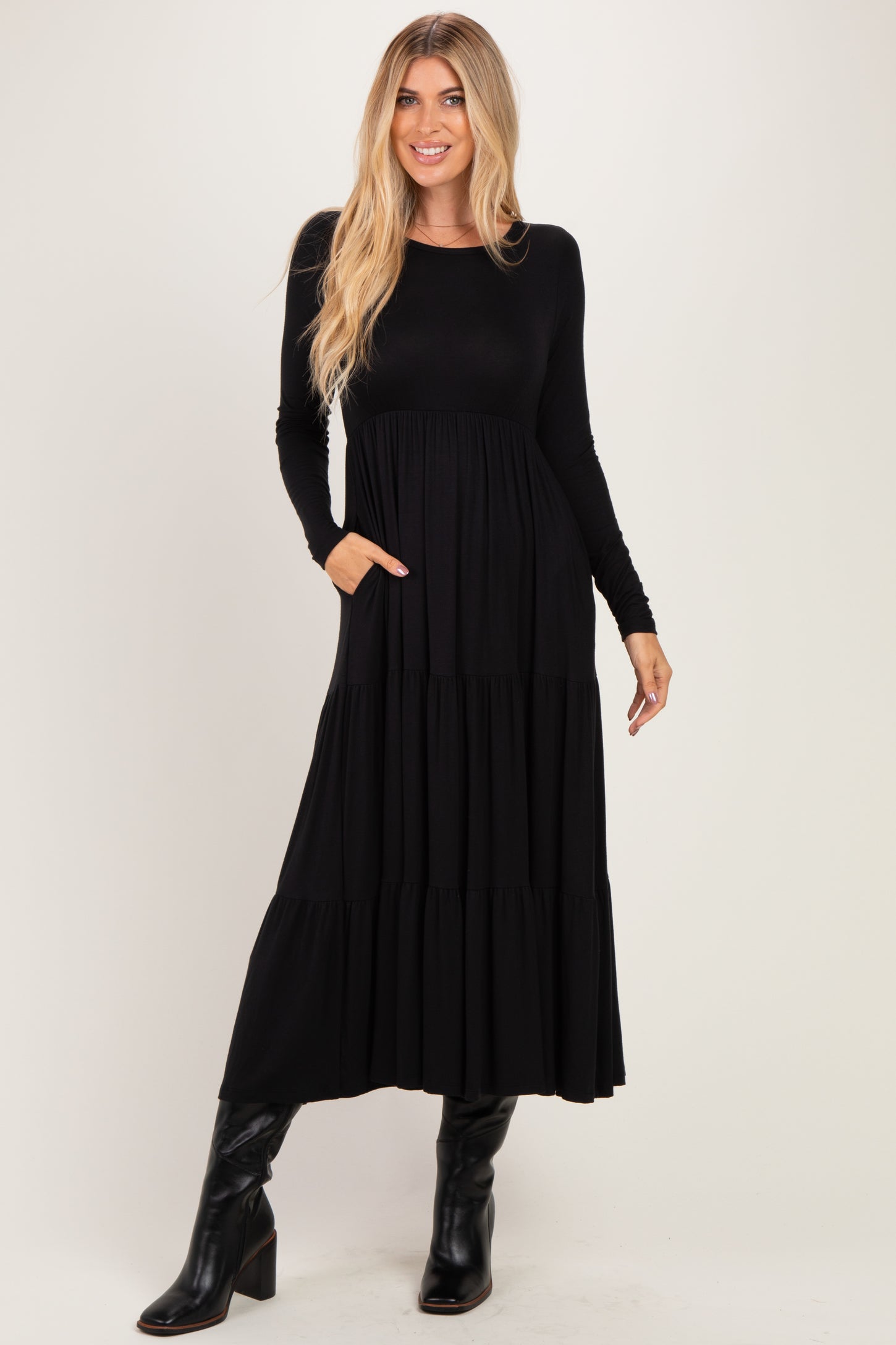woman wearing a black long sleeve maxi dress with a tiered design and pockets, paired with knee-high black boots
