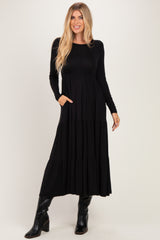 woman wearing a black long sleeve maxi dress with a tiered design and pockets, paired with knee-high black boots