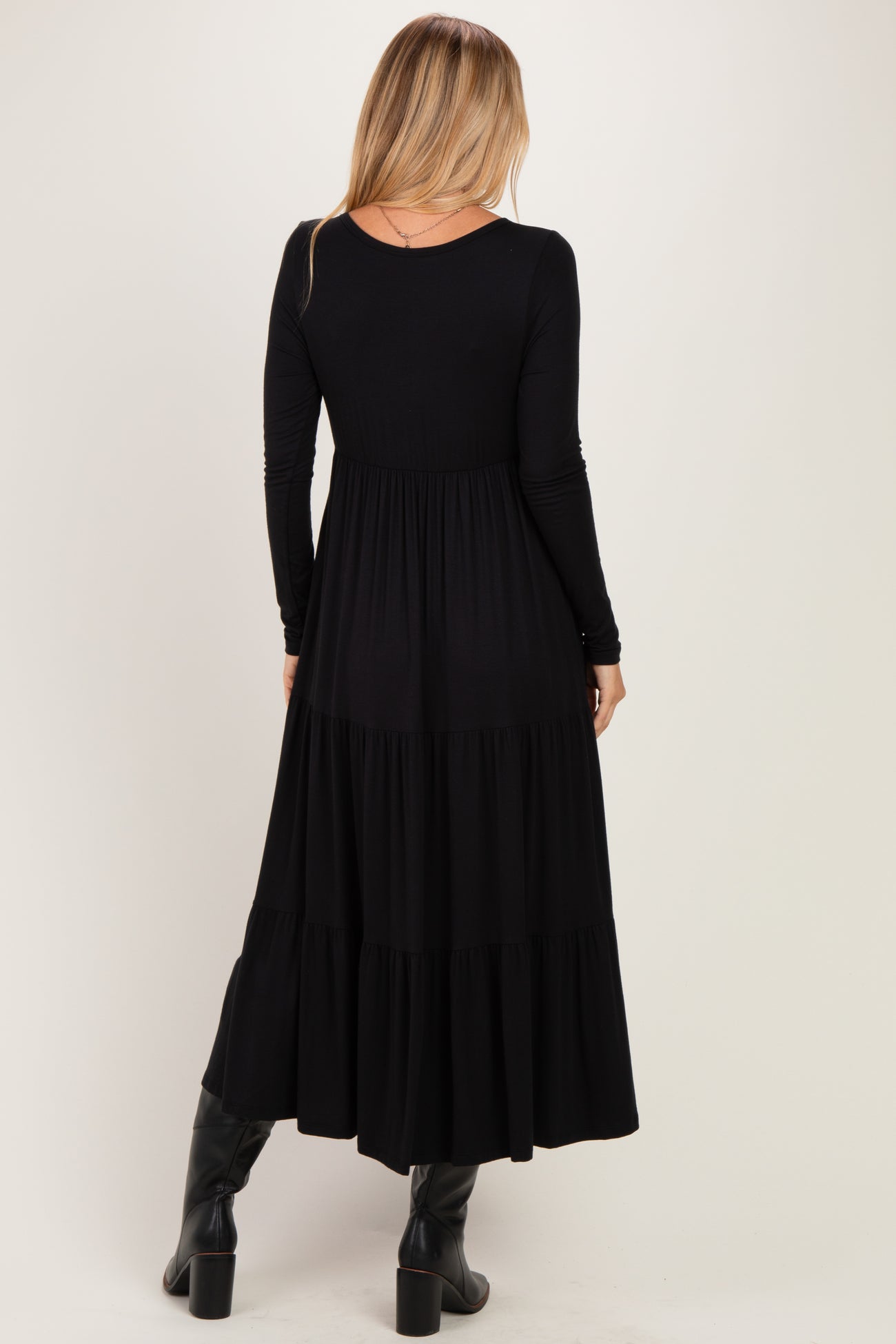woman wearing a black long sleeve maxi dress with a tiered skirt and a fitted bodice, seen from the back