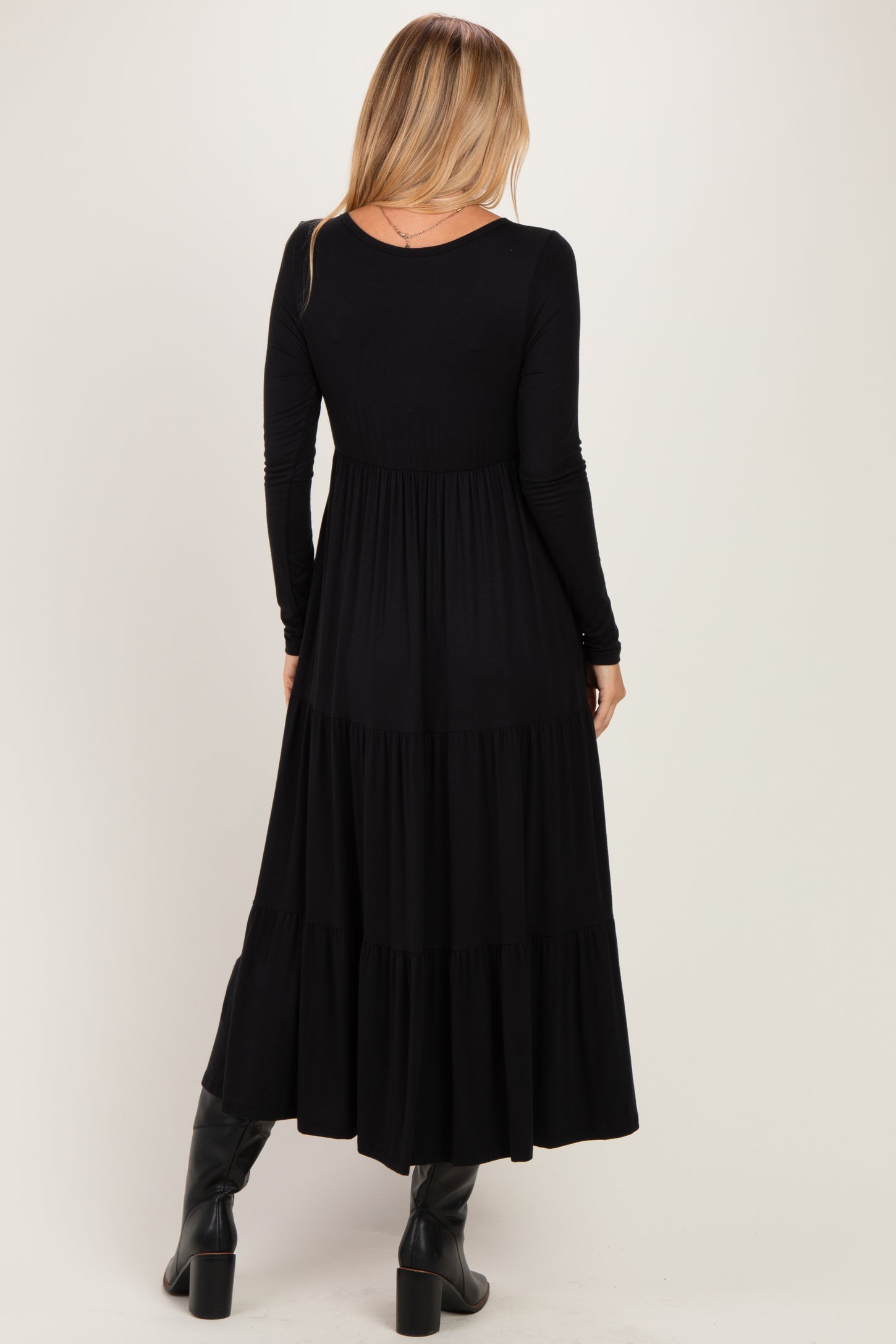woman wearing a black long sleeve maxi dress with a tiered skirt and a fitted bodice, seen from the back