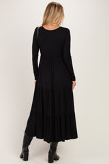 woman wearing a black long sleeve maxi dress with a tiered skirt and a fitted bodice, seen from the back