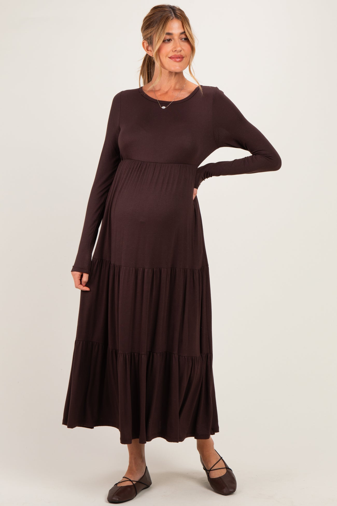 woman wearing a dark brown long sleeve maternity dress with tiered skirt and visible baby bump