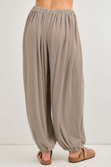 woman wearing light brown striped wide-leg pants with an elastic waistband and gathered cuffs, standing from the back