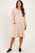 woman wearing a beige maternity dress with long puff sleeves and pockets, showcasing a visible baby bump