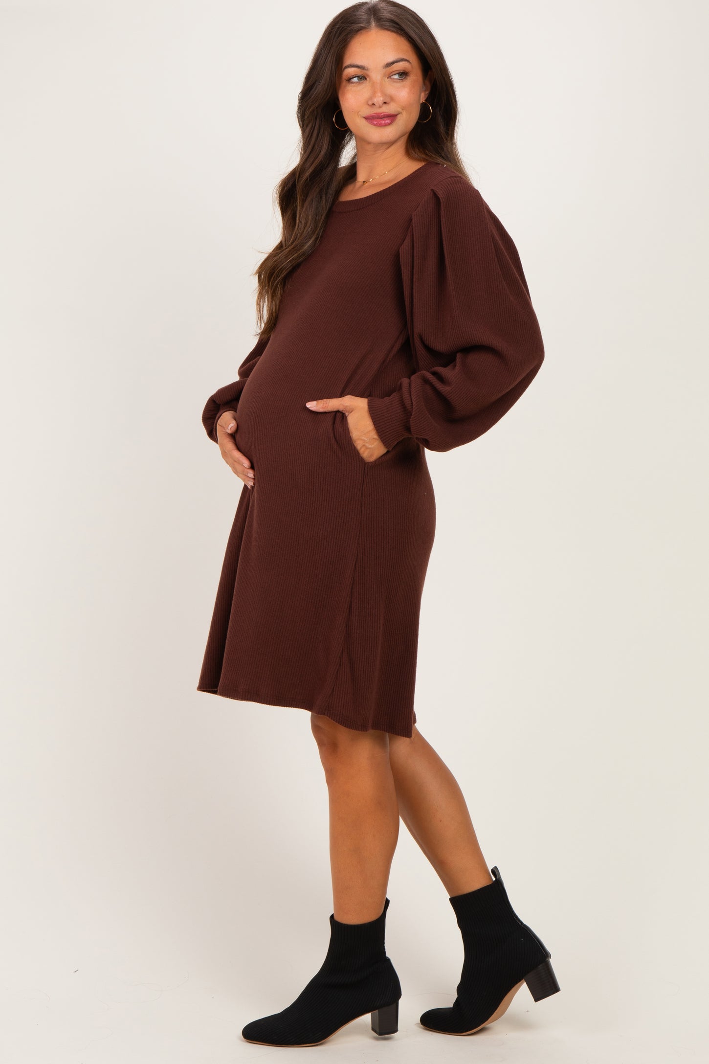 woman wearing a brown maternity dress with long puff sleeves and pockets, showing her baby bump
