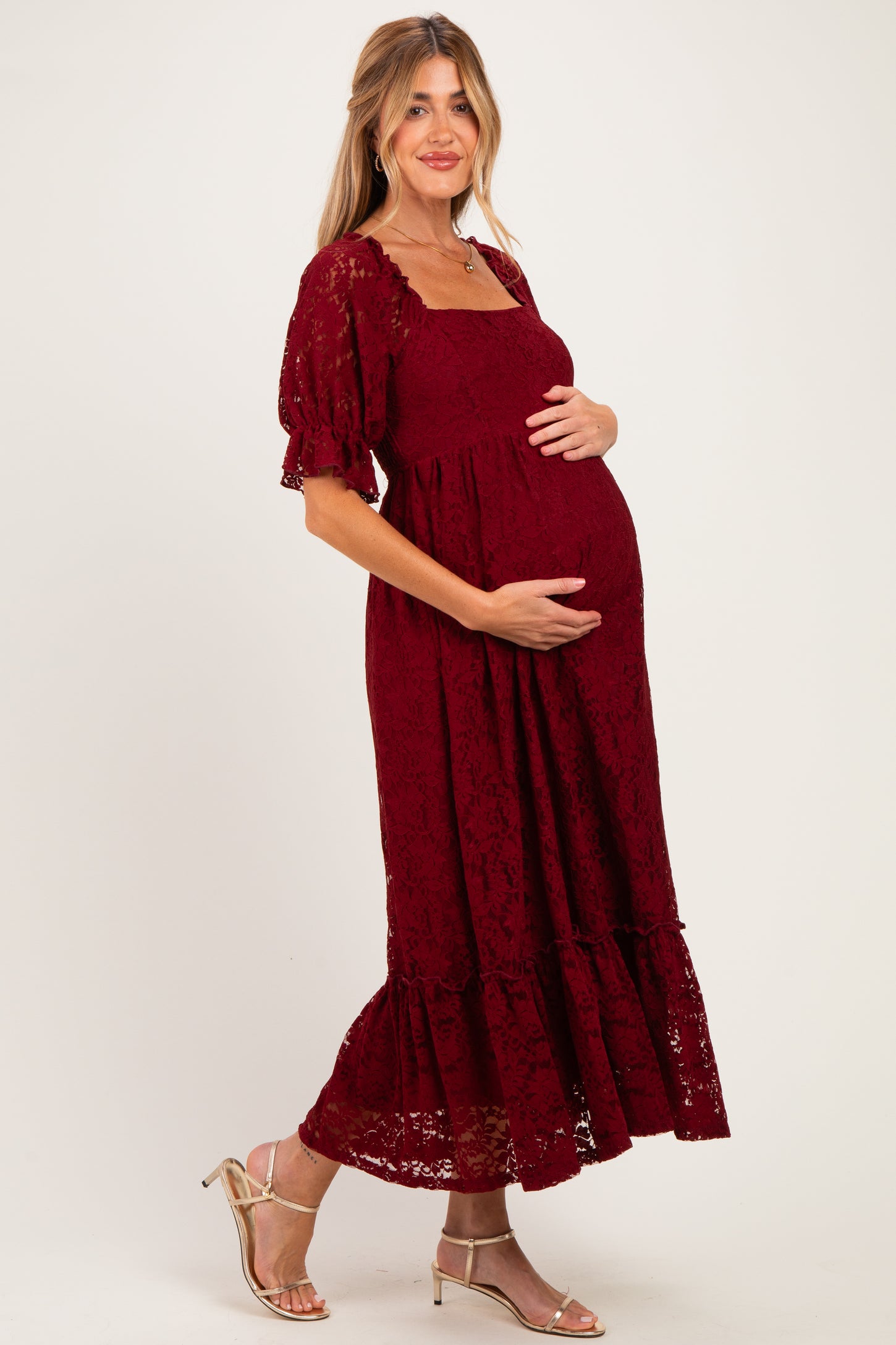 woman wearing a burgundy lace maternity dress with short puff sleeves and a flowing skirt, holding her baby bump