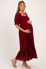 woman wearing a burgundy lace maternity dress with short puff sleeves and a flowing skirt, holding her baby bump