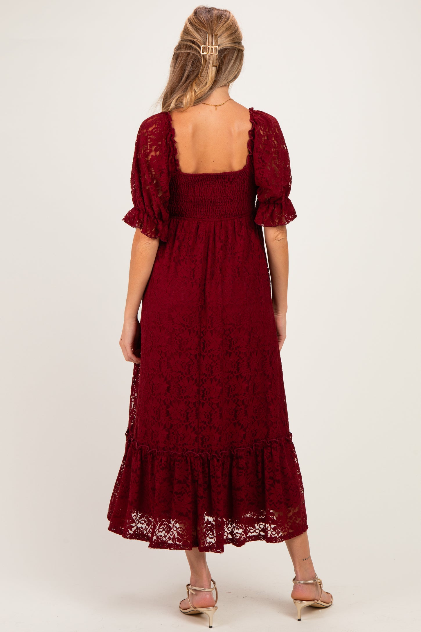 woman wearing a burgundy lace maternity dress with a smocked bodice and ruffled hem, showing her back