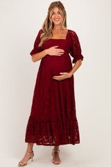 woman wearing a burgundy lace maternity dress with puff sleeves and ruffle hem, holding her baby bump