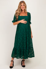 woman wearing a dark green lace maternity dress with short puff sleeves and a tiered skirt, holding her baby bump