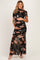 woman wearing a black floral print maternity dress with ruching and a flowing skirt, cradling her baby bump