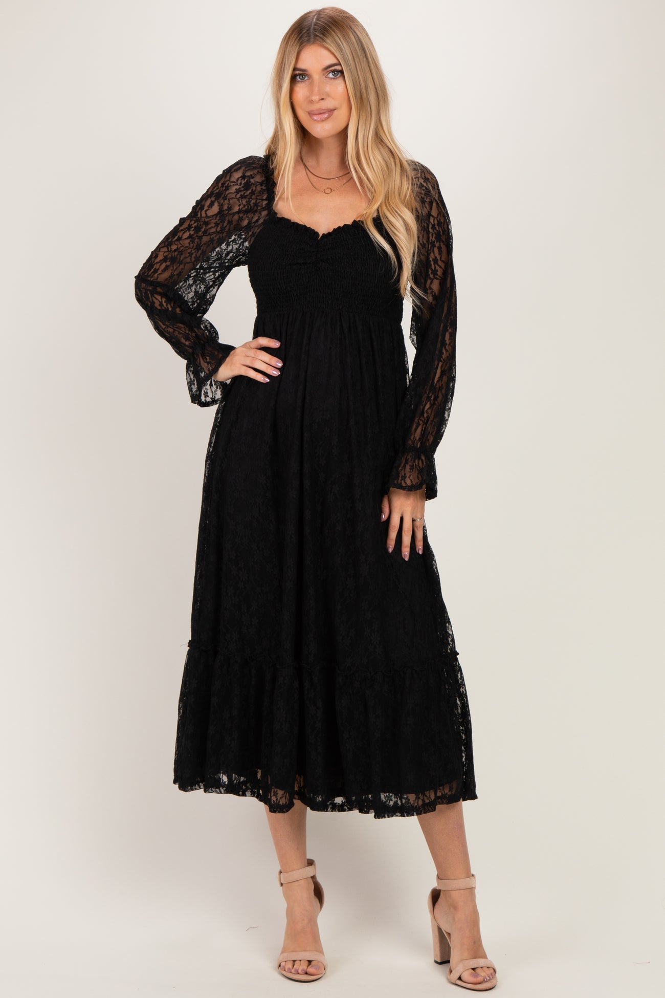 woman wearing a black lace maxi dress with smocked bodice and long sleeves, posing with an elegant stance