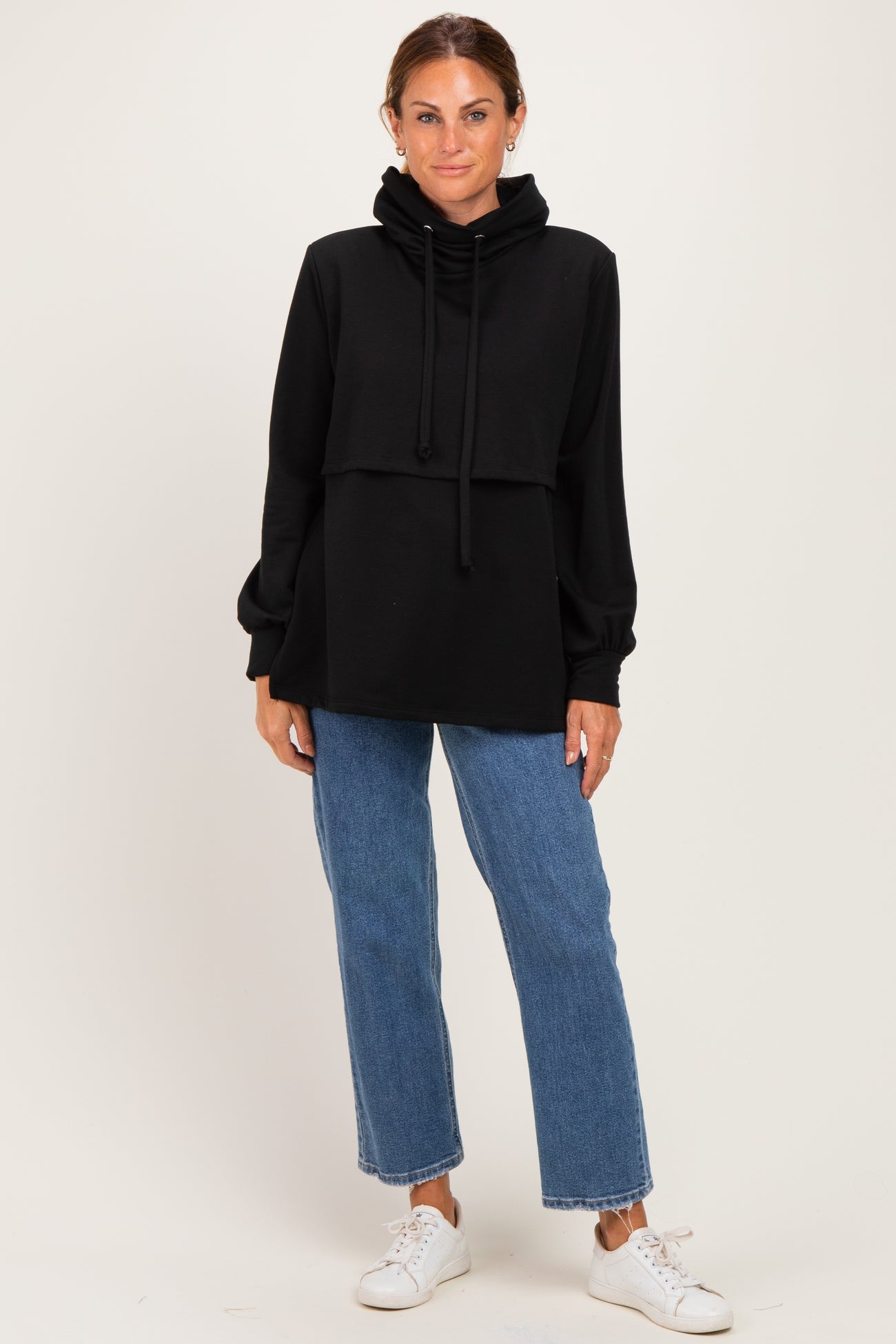 woman wearing a black cropped hoodie with long sleeves and a relaxed fit, styled with high-waisted blue jeans and white sneakers