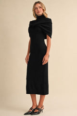 woman wearing a black knit midi dress with a high neck and draped shoulders, styled with black pointed-toe heels