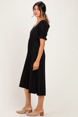 woman wearing a black short sleeve midi dress with a gathered waist and side pockets, standing sideways
