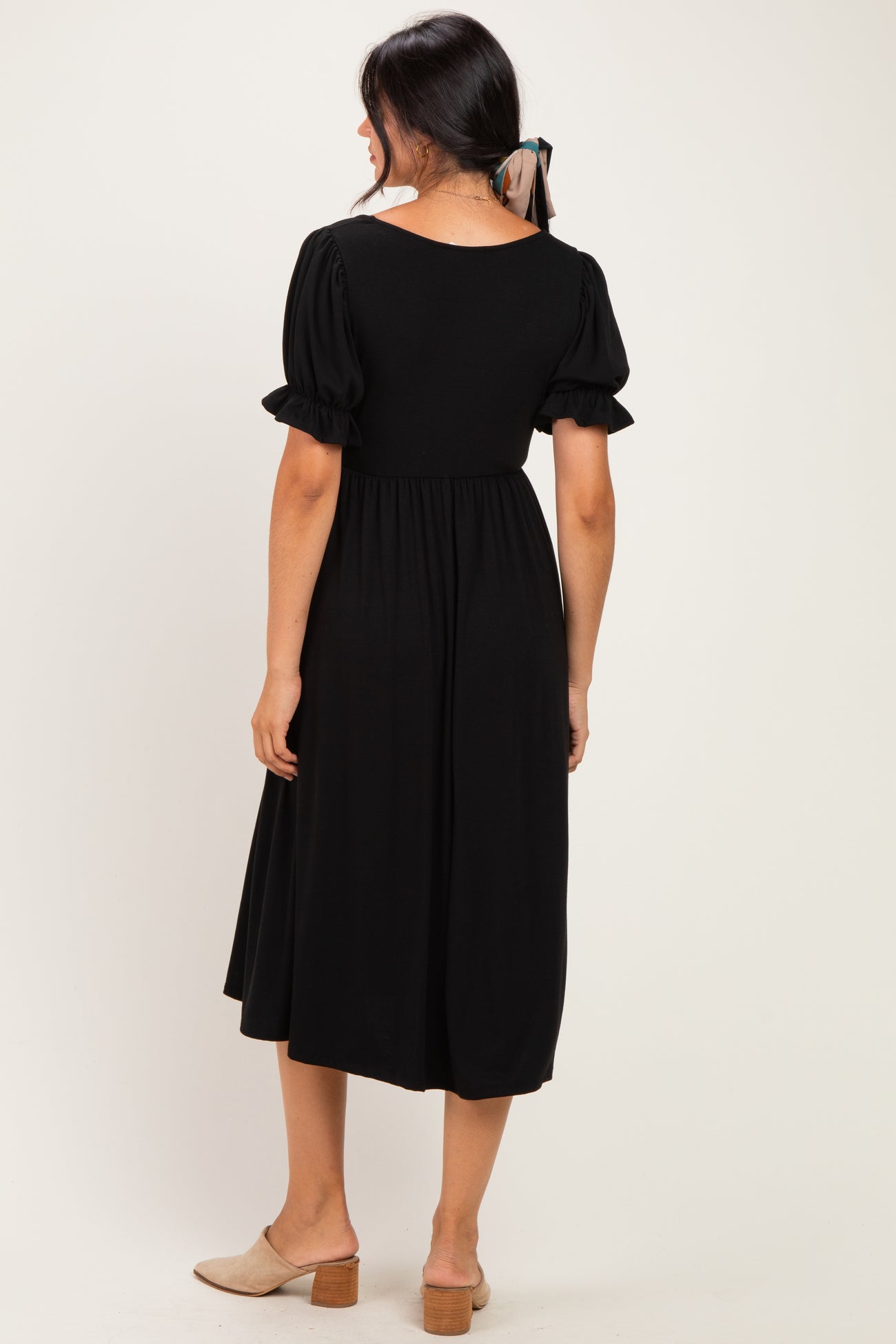 woman wearing a black midi dress with puff sleeves, showing the back view and paired with tan slip-on shoes
