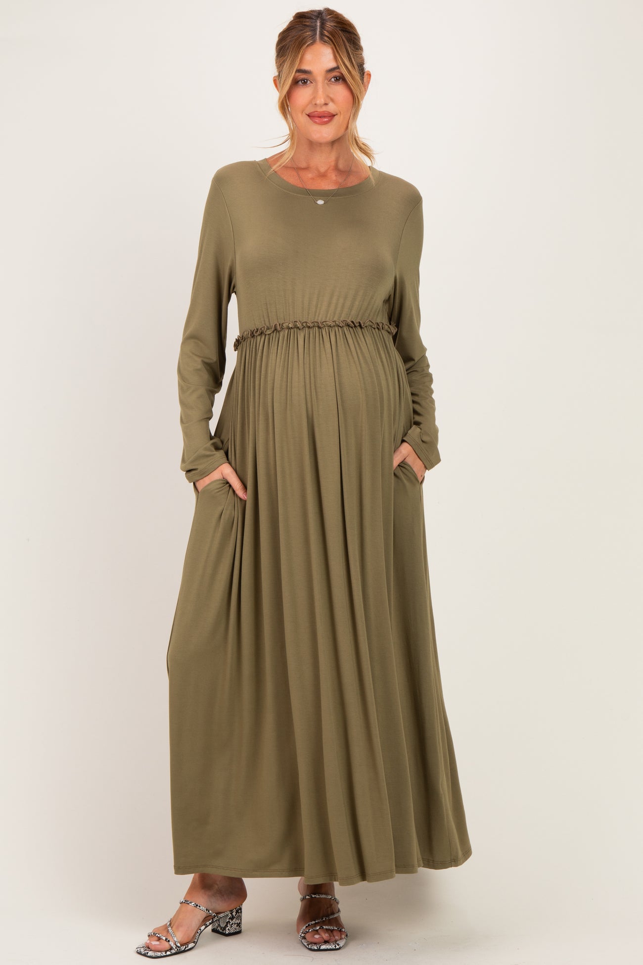 woman wearing an olive green long sleeve maternity dress with a cinched waist and pockets, revealing a baby bump