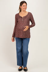 woman wearing a brown maternity long sleeve top with floral print and buttons, holding her baby bump, paired with blue jeans