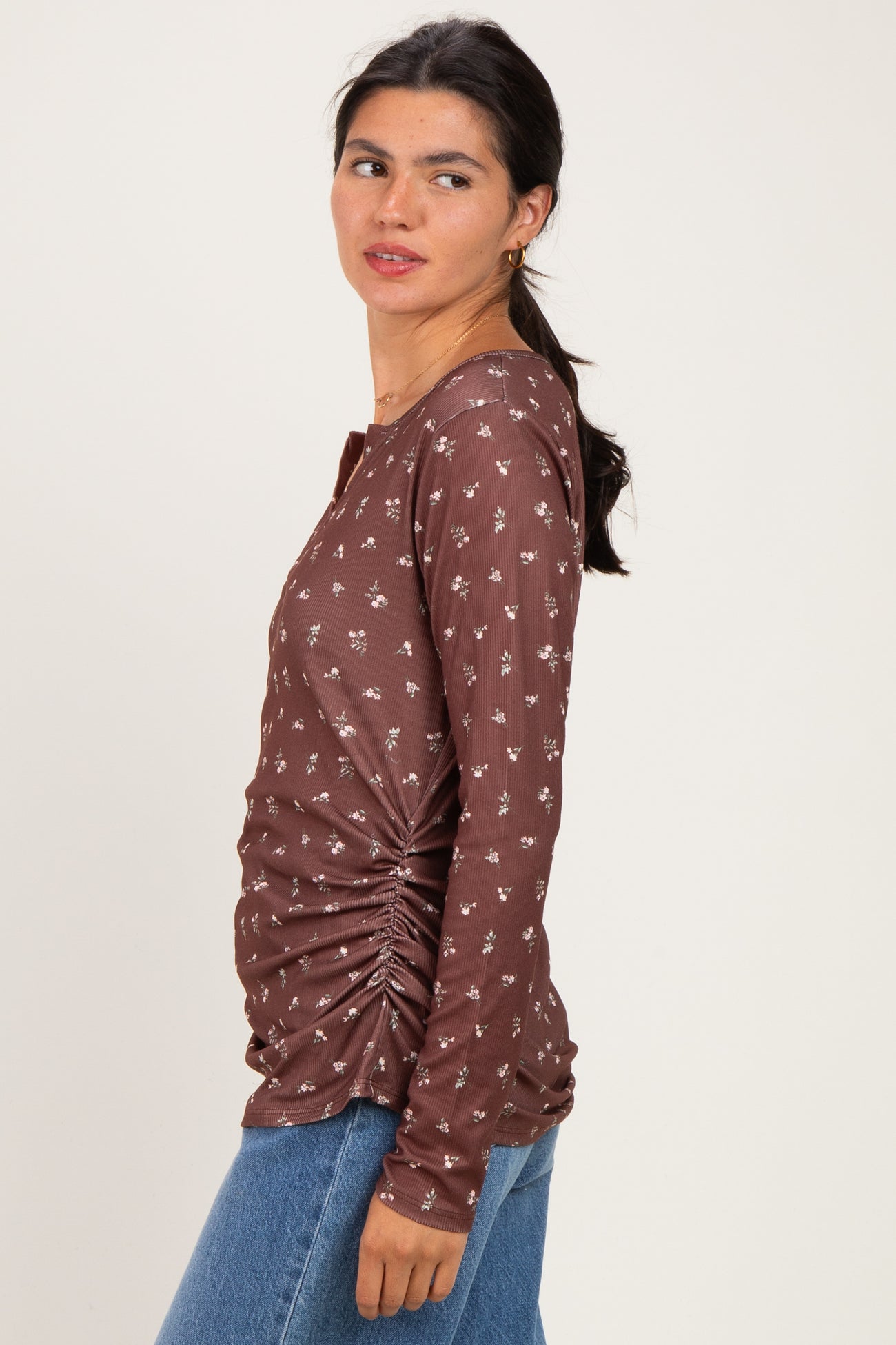 woman wearing a brown long sleeve top with floral print and side ruching, styled with blue jeans