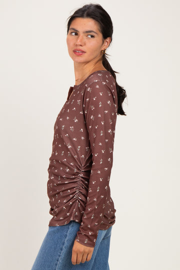 woman wearing a brown long sleeve top with floral print and side ruching, styled with blue jeans