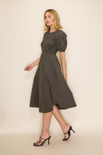 woman wearing an olive green puff sleeve midi dress with a fitted bodice and flared skirt, walking confidently
