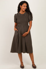 woman wearing a dark green short sleeve maternity dress with a smocked bodice and pockets, holding her baby bump