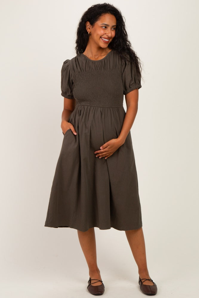 woman wearing a dark green short sleeve maternity dress with a smocked bodice and pockets, holding her baby bump