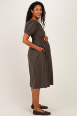 woman wearing a dark green maternity dress with puff sleeves and pockets, showing her baby bump