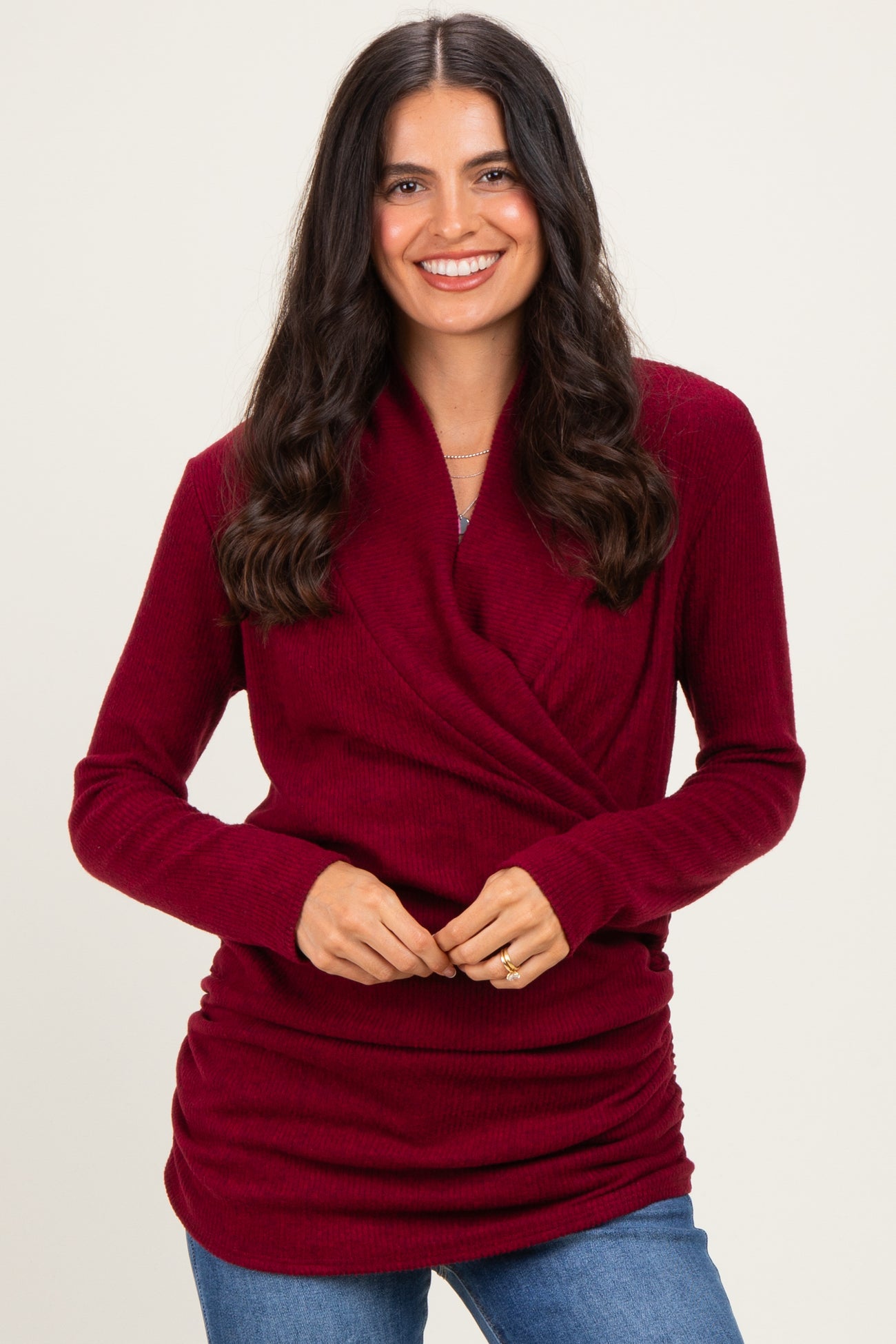 woman wearing a burgundy long sleeve wrap top with ribbed texture and ruched detailing, smiling at the camera