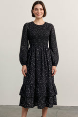 woman wearing a black floral long sleeve dress with a smocked bodice and tiered ruffle hem