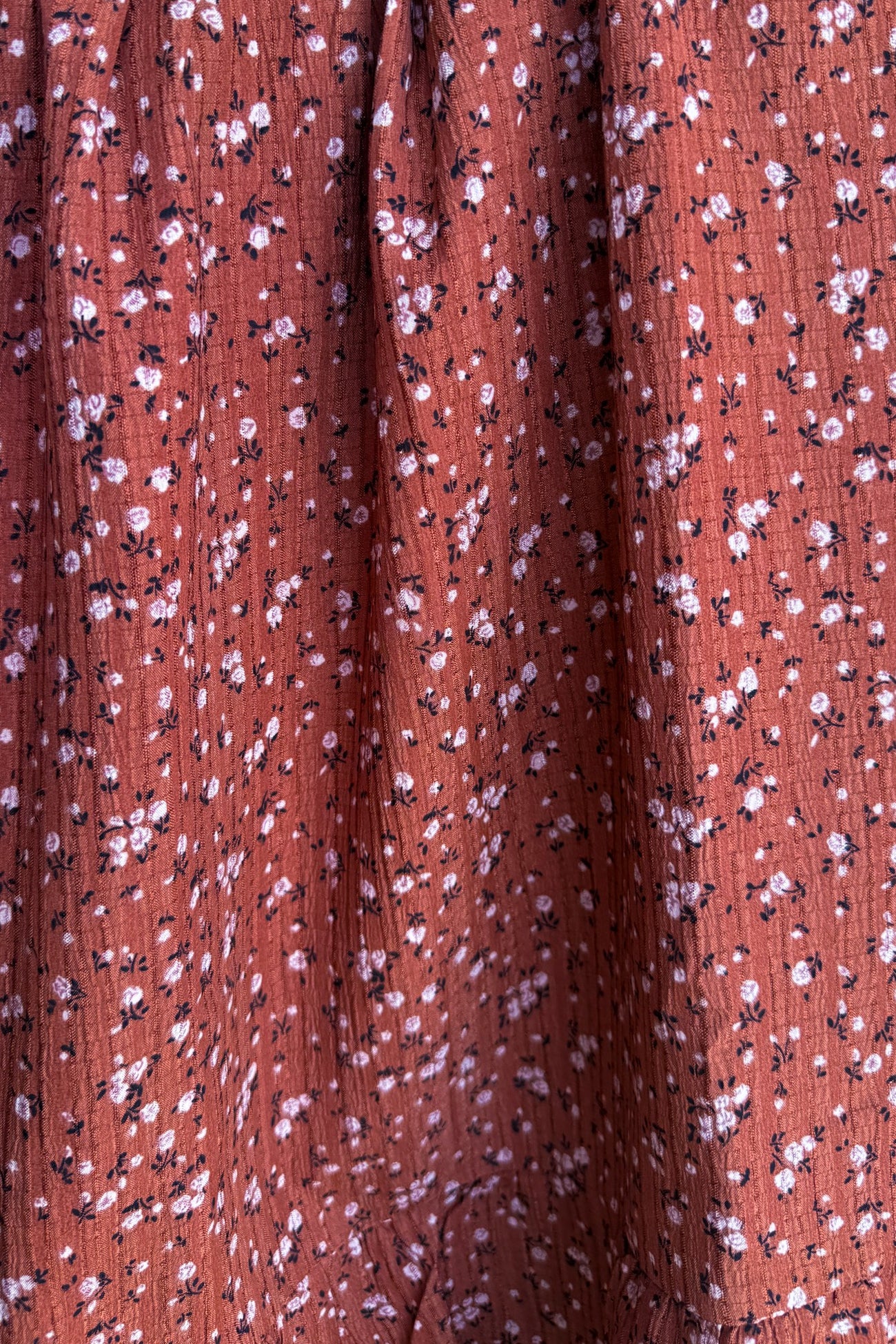 rust floral print fabric with small pink and white flowers on a textured background
