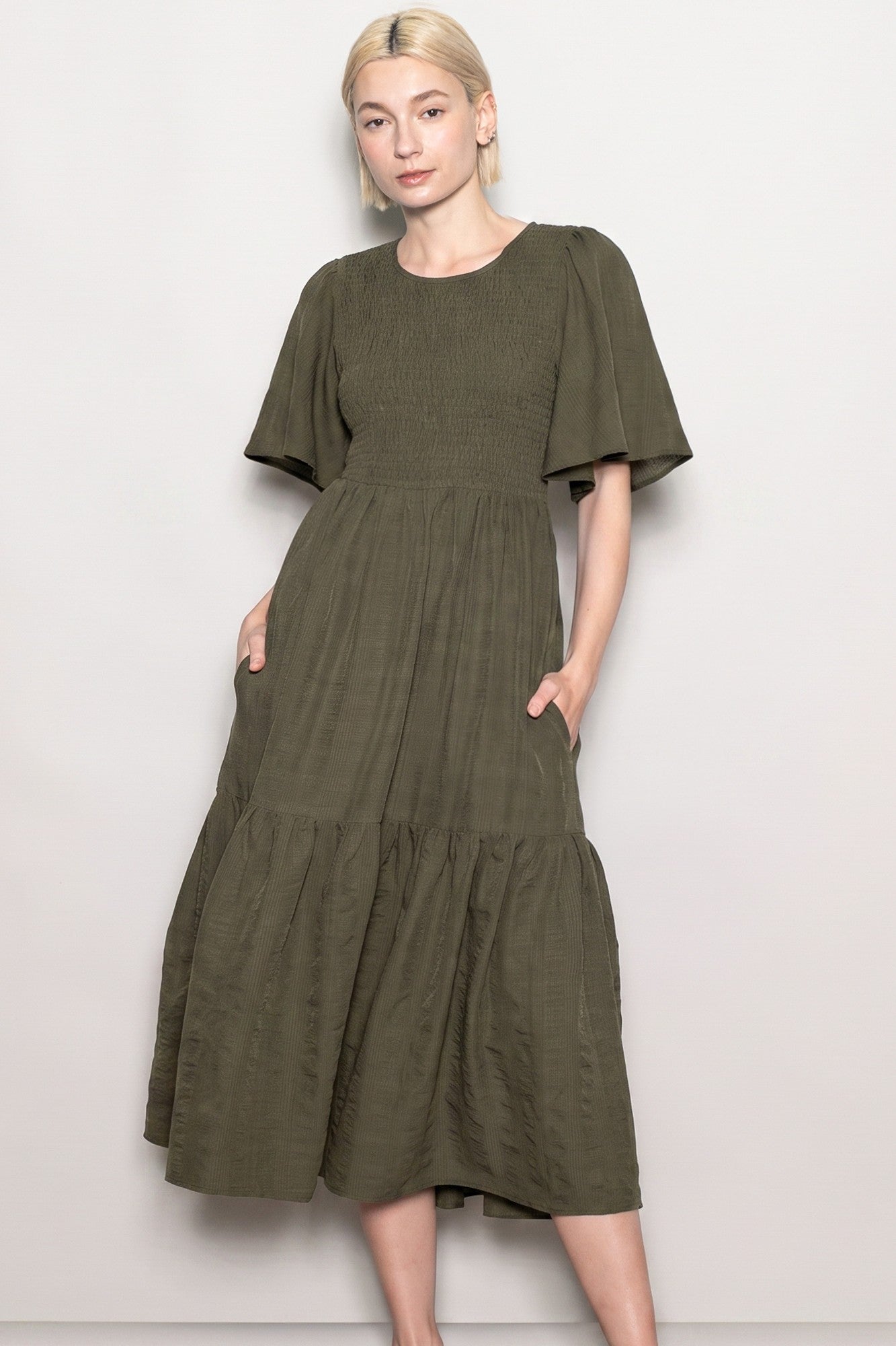 woman wearing an olive green smocked midi dress with short flutter sleeves and pockets