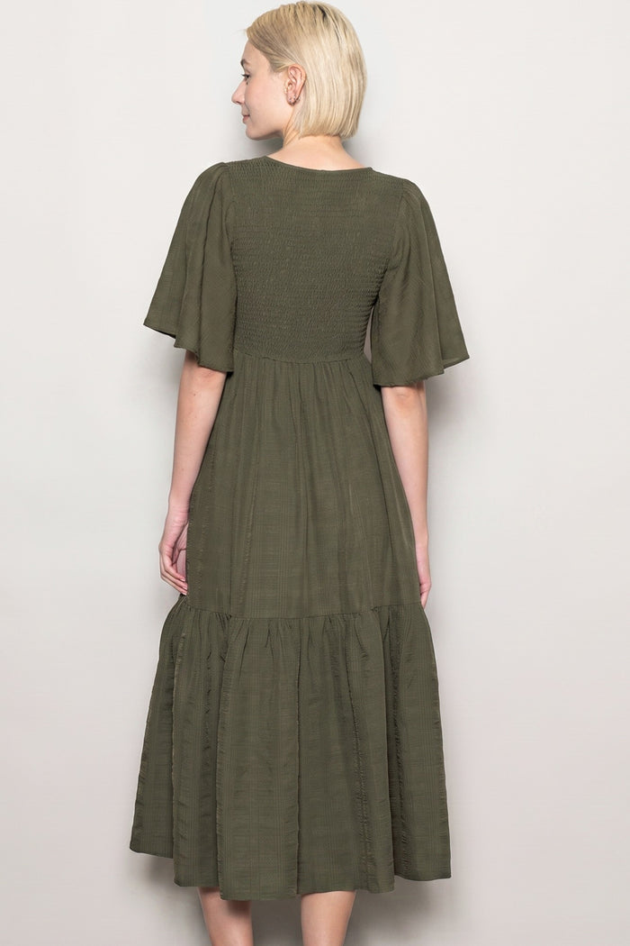 woman wearing a dark green midi dress with short flutter sleeves and a tiered skirt, viewed from the back